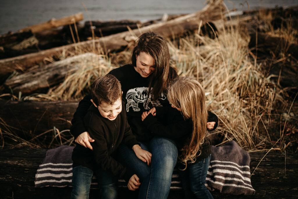 Woman sitting with two children on driftwood logs at the beach