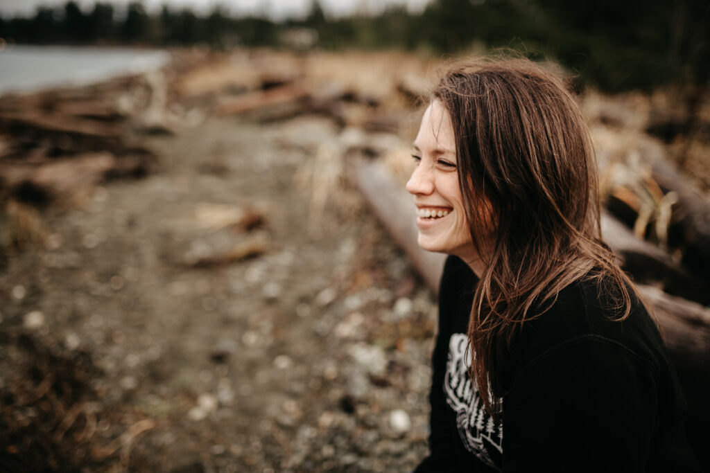 Tiffany Dawn smiling while sitting on driftwood at the beach in Campbell River, BC